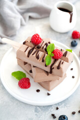 Homemade chocolate ice cream (popsicles) with fresh raspberry and blueberry on a plate on a gray background. copy space.