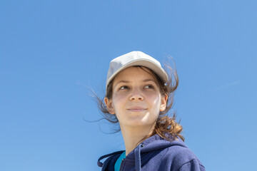 Natural face portrait of a young caucasian woman, no retouching skin, no color correction. Close-up girl outdoor portrait on a sky background, brunette in baseball cap, naturalness. Copy space. - 466119451