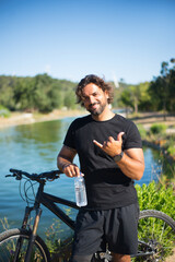 Portrait of sporty person with disability with bicycle. Man with mechanical leg standing near pond...