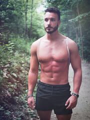 Young man shirtless outdoors hiking with backpack on shoulder