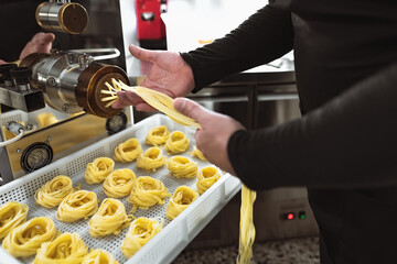 Closeup male hands preparing fresh fettucine using machine inside pasta factory