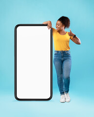 Black woman standing near giant cellphone, showing thumb up, offering space for your website or advertisement, mockup