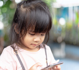 A headshot portrait select focus of a cheerful baby Asian woman, a cute toddler little girl with adorable bangs hair, playing mobile phone and don't look to the camera.