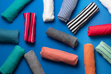 close up of rolled colorful t shirt clothes on blue table background, travel prepare concept