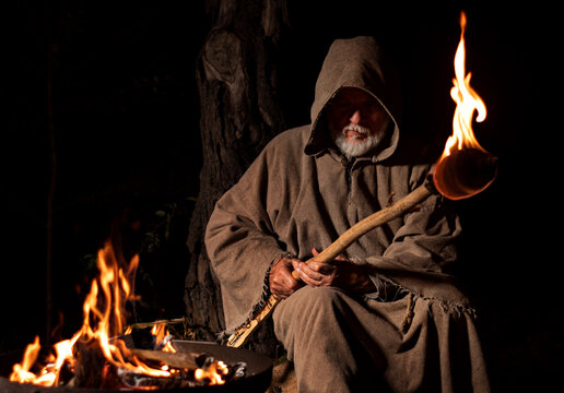 Old medieval monk by the fire with torch