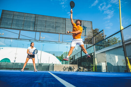 Mixed padel match in a blue grass padel court - Beautiful girl and handsome man playing padel outdoor