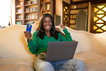 Excited black lady with laptop and credit card gesturing YES, happy over huge discount in online...