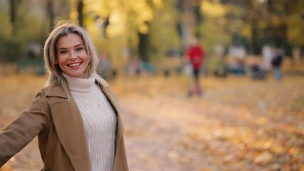 Attractive mature blond woman walking down the park turns around with flying hair and looking at the camera outdoors Happy relaxed female walking on the autumn park enjoying beautiful time - Powered by Adobe