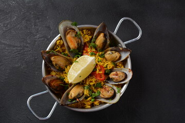 Traditional spanish seafood paella in the fry pan. Spanish paella with clamps, mussels, and fresh lemon wedges