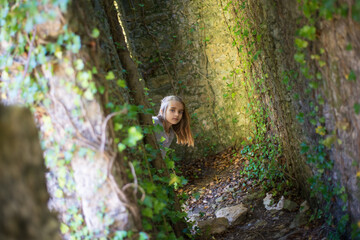 Cute little girl in old castle at forest. Curious girl with long fair hair peeking out from corner....