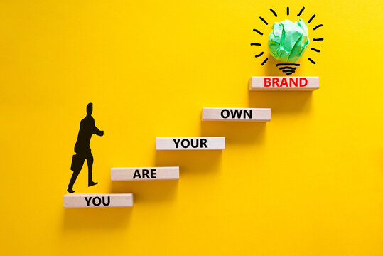 You are your own brand symbol. Wooden blocks with words You are your own brand. Beautiful yellow background, copy space. Businessman icon, light bulb. Business, you are your own brand concept.