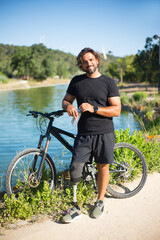Portrait of person with disability with bicycle. Man with mechanical leg standing near pond on...