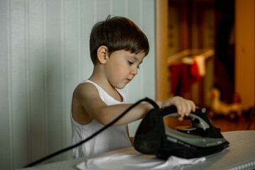 a five-year-old boy helps his mother around the house, the child irons clothes with an iron