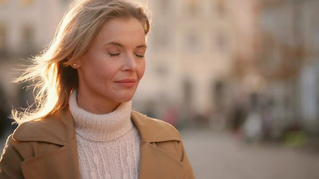 Blond smiling mature woman with flying blond hair in blowing wind looking at camera. Portrait of caucasian woman with blond hair and blue eyes. High quality 4k footage