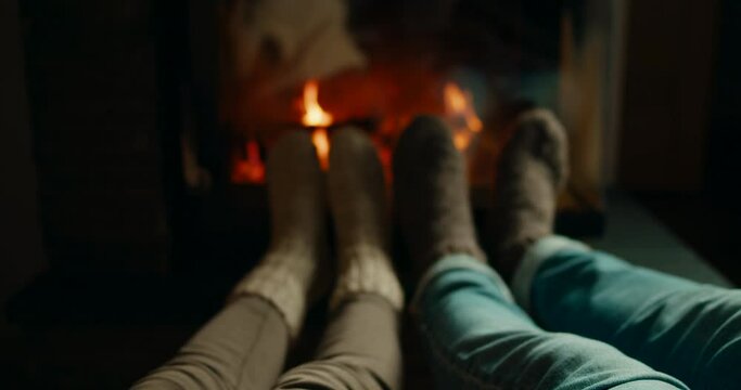 Close up of Clinking Glasses with Red Wine with Fireplace at Background. Loving Couple in Woolen Socks Celebrates Christmas Holiday or St Valentine Day at Winter Evening. 4K slider pan shot