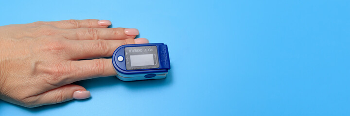 Senior Woman Using Pulse Oximeter, Measuring Oxygen Saturation. Human hand pulse oximeter used to measure pulse rate and oxygen levels with medical blue background with copy space