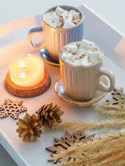 Obraz na płótnie Canvas two cups of hot drink with marshmallows and christmas decor on white wooden tray