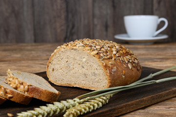 Homemade sliced bread on dark cutting board, cup and ears on wooden table
