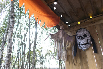 halloween decorations with ghost and a huge skeleton head on a wooden wall with birch trees in the background