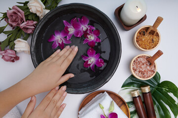 Obraz na płótnie Canvas Woman soaking her hands in bowl of water and flowers, Spa treatment and product for female feet and hand spa, massage pebble, perfumed flowers water and candles, Relaxation. Flat lay. top view.