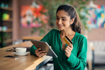 Cheerful indian lady banking online, using digital tablet at cafe