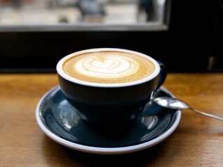 a cup of cappuccino on the wooden table by the window in a nice cafe