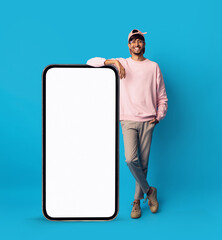 Cheerful young middle-eastern man standing by huge cellphone, mockup