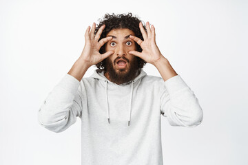 Shocked hispanic man widen his eyes in awe, cant believe, looking with disbelief and amazement at camera, standing startled over white background