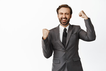 Enthusiastic lucky businessman winning and celebrating, shouting with joy and fist pumps, triumphing, achieve goal, success, white background