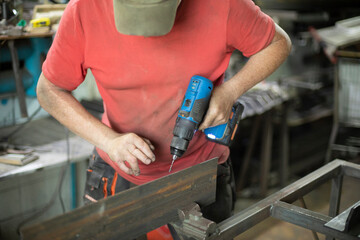 A worker in a gray cap and a red T-shirt works with a screwdriver. Close-up, front view. Metal construction.