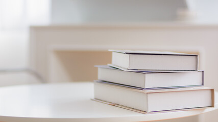 Books stacked on table in warm white room.