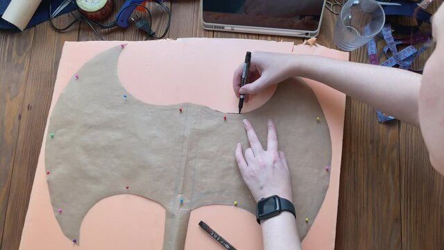 Girl outline sheet of paper with marker with silhouette of hatchet on piece of styrofoam. Cosplayer makes celtic axe on wooden table for festival or performance.