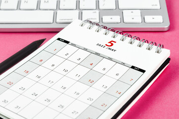 May 2022 desk calendar with pencil on pink background.