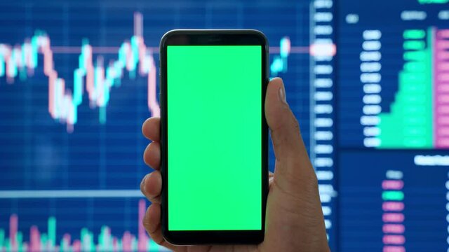 Male cryptocurrency trader investor analyst hand holding cell phone with green mockup screen doing stock market data price graphs analysis using cryptocurrency trading mobile app, stock application.