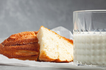 Food photo composition. Fresh white bread bun with sugar on a gray background. Nearby is a glass of milk.