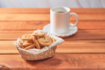 Palm cookies or puff pastry ears and a cup of coffee on a wooden table.