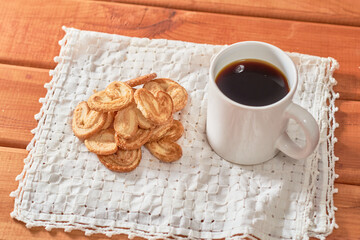 Palm cookies or puff pastry ears and a cup of coffee on a wooden table.