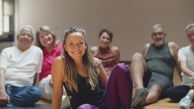 Long shot of female teacher sitting with dancing group on floor. Slow motion of senior people resting after dance class with instructor, looking at camera and smiling. Hobby, emotion concept