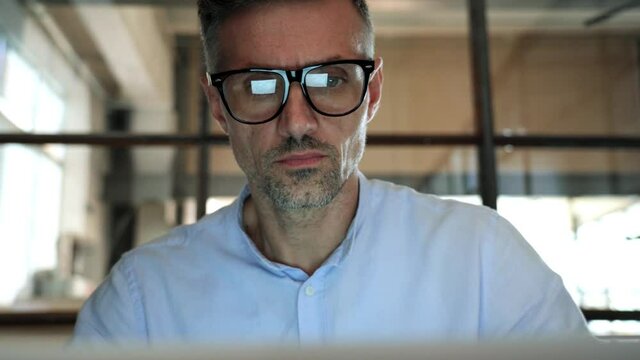 Mature concentrated business man trader wearing eyeglasses working looking at laptop computer screen reflecting in glasses thinking analyzing online trading market finance digital data. Close up view