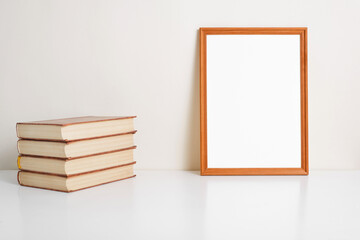 Vertical portrait frame mock up. Wooden picture frame template with empty space, books on table indoors. Simple minimal interior decor layout