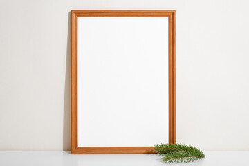 Frame mockup and twig of pine on table indoors. Portrait vertical frame template with blank space, simple minimal interior decor. Christmas or Happy New Year layout concept
