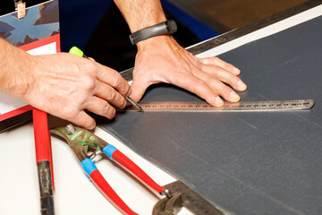 A worker marks out a sheet of roofing iron with a pencil and a metal ruler. Close-up of a worker's hands.