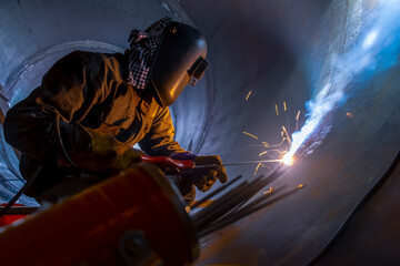MMA welding. A welder welds large diameter pipes with manual electric arc welding.
