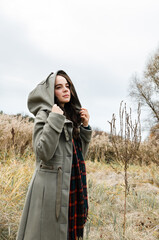 Young dreamy woman with a hood on standing in the dry grass field looking away during autumn season.
