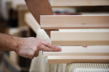 The man is sanding wood with sand paper in part of the furniture making process