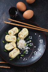 Black plate with sliced tamagoyaki or sweetened japanese egg roll, vertical shot on a dark brown stone surface