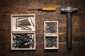 Old hammer, screwdriver, nails and screws in the boxes on the wooden flat lay workbench background.