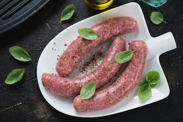 Above view of fresh uncooked seasoned sausages on a white shovel-shaped plate, studio shot on a dark brown stone surface