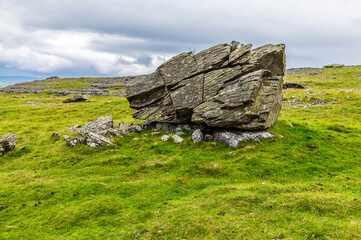 A view of a glacial erratic perched on a limestone base on the southern slopes of Ingleborough, Yorkshire, UK in summertime