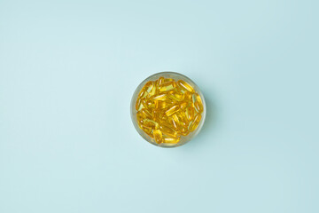 Omega 3 capsules lying in a bowl on a blue background